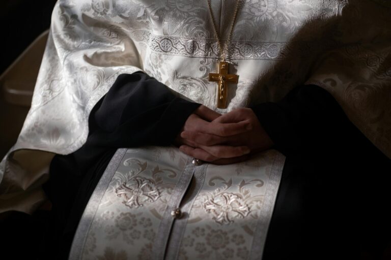 Intimate close-up of orthodox priest's hands in traditional religious robes, highlighting the intricate fabric and crucifix.